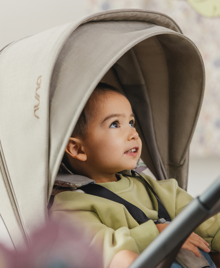 Child looking out with wonder from under the canopy of Nuna's TRIV next stroller