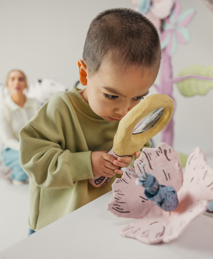 Child examines papier maché flower with magnifying glass