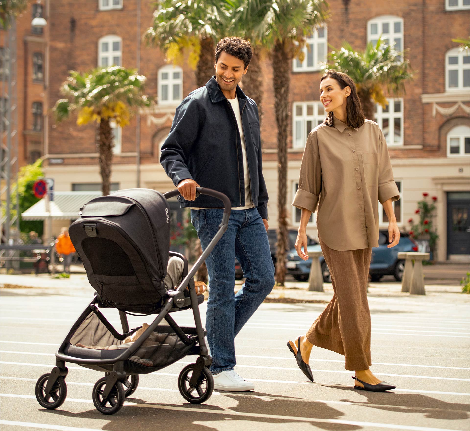 A couple walks through a square smiling and casually pulling a Nuna SWIV stroller