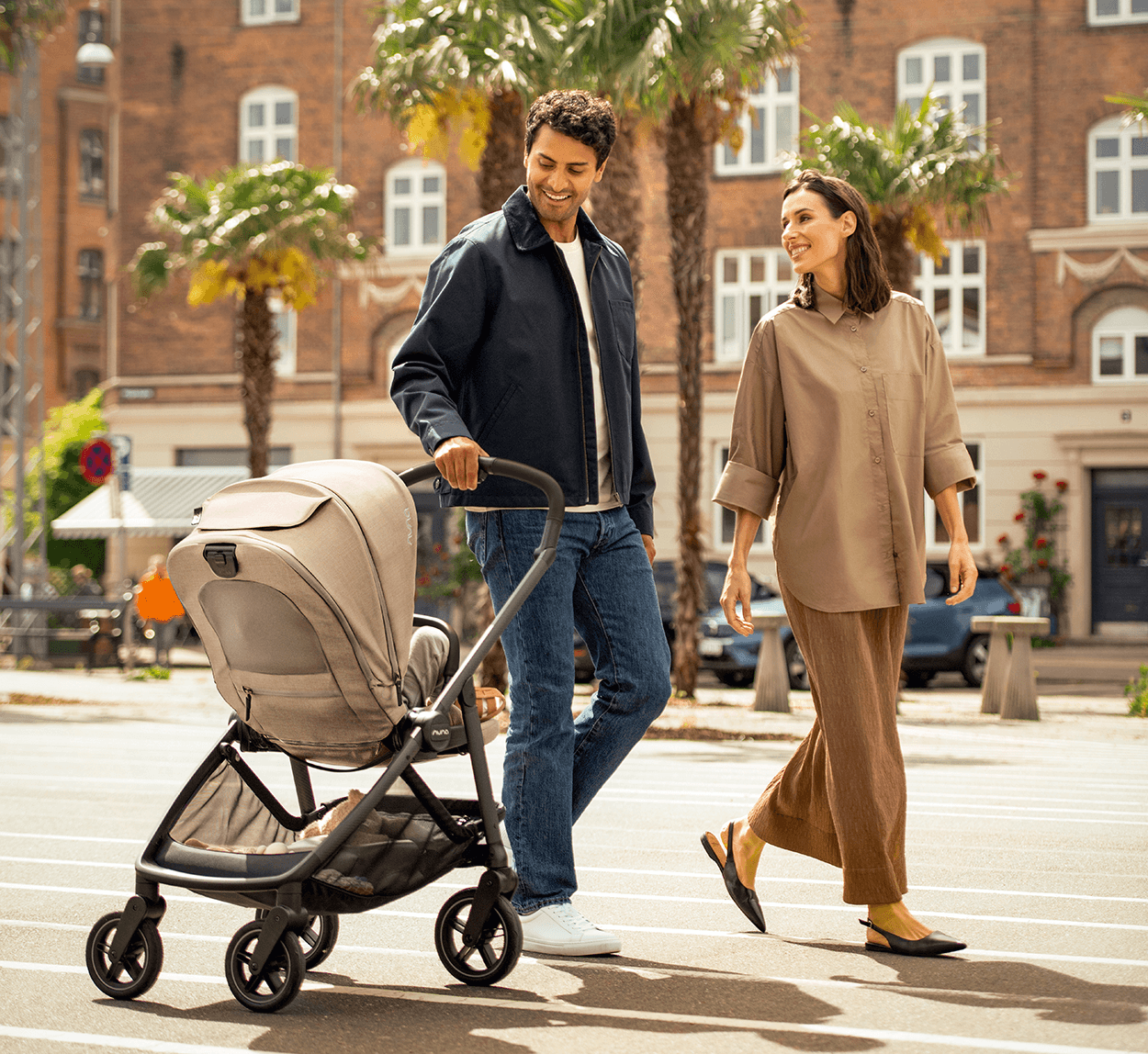 A couple walks through a square smiling and casually pulling a Nuna SWIV stroller